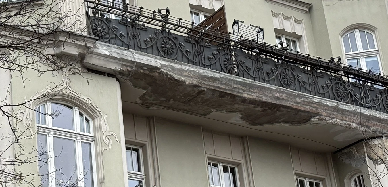 Zniszczony balkon międzywojennej kamienicy w Poznaniu z widocznymi ubytkami hydroizolacji i korozją obróbek blacharskich – stan przed renowacją.webp